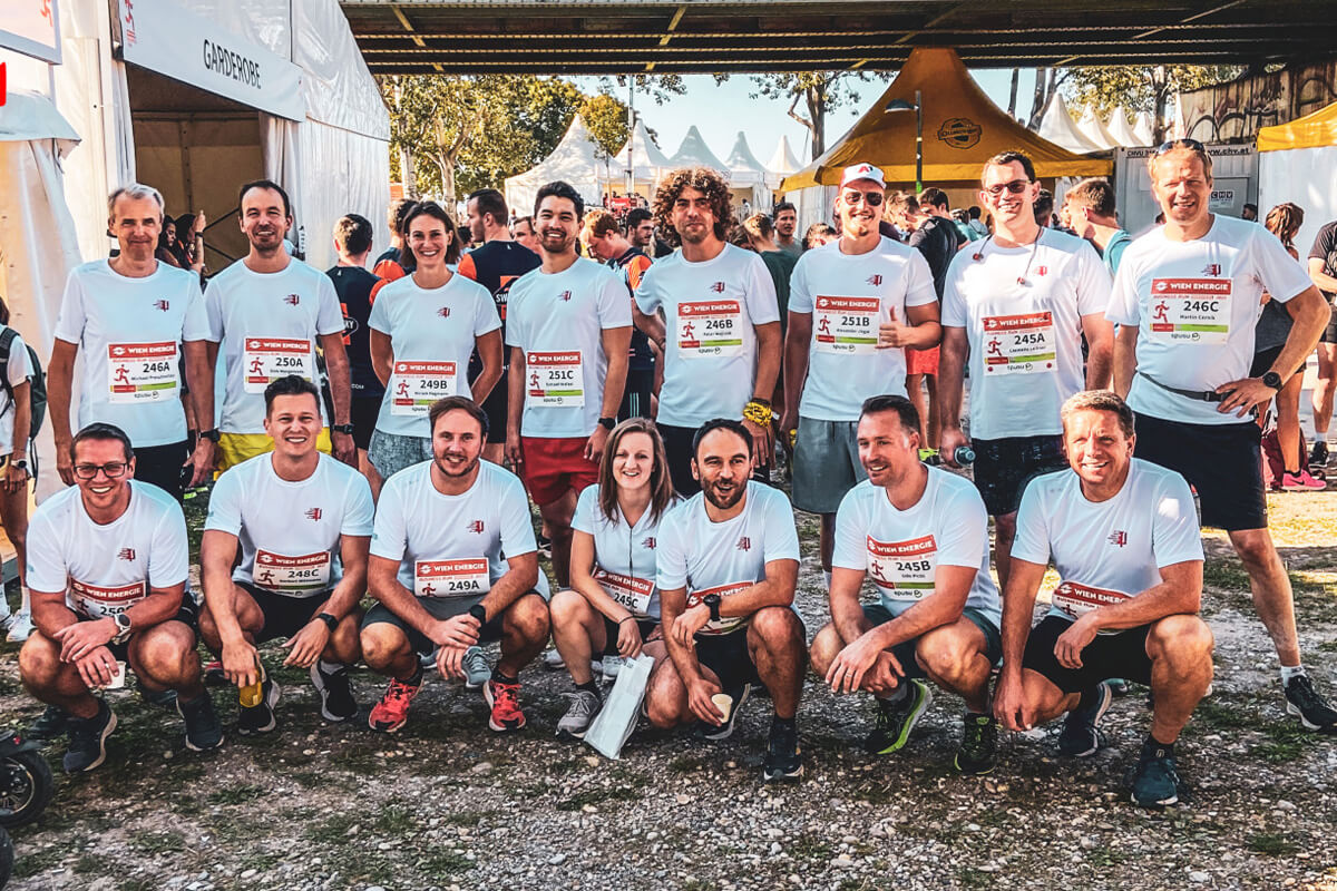 Eine Gruppe von 15 Menschen in weißen Shirts mit Startnummern darauf und roten Shorts steht zusammen und lächelt in die Kamera.